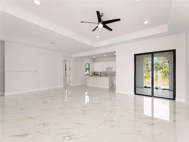 unfurnished living room featuring ceiling fan, sink, and a raised ceiling