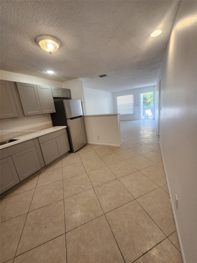 kitchen with light tile patterned floors, a textured ceiling, stainless steel fridge, and gray cabinetry