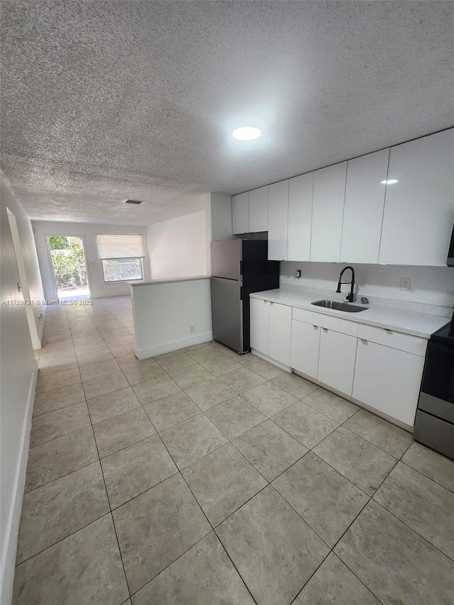 kitchen featuring sink, white cabinets, stainless steel fridge, and electric stove