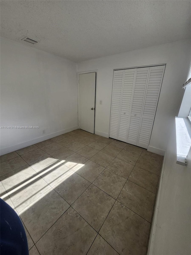 unfurnished bedroom featuring a textured ceiling, light tile patterned floors, and a closet