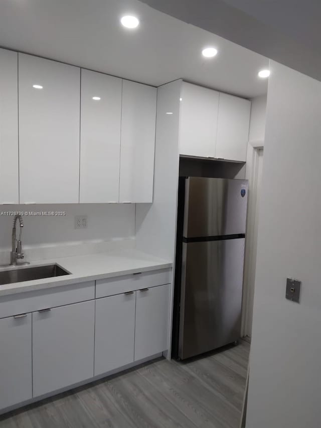 kitchen featuring white cabinets, light wood-type flooring, stainless steel fridge, and sink