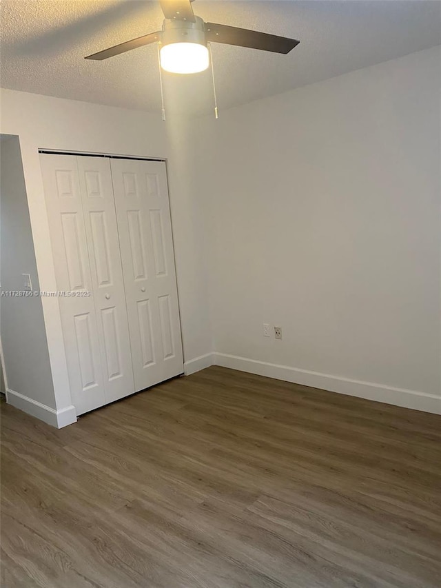 unfurnished bedroom featuring ceiling fan, a closet, dark wood-type flooring, and a textured ceiling