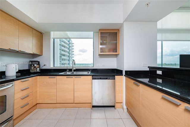 kitchen featuring light tile patterned floors, appliances with stainless steel finishes, light brown cabinets, dark stone countertops, and sink