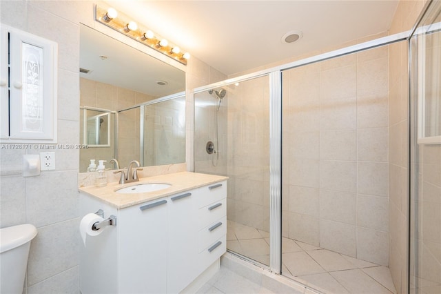 bathroom featuring toilet, vanity, tile walls, tile patterned flooring, and a shower with door