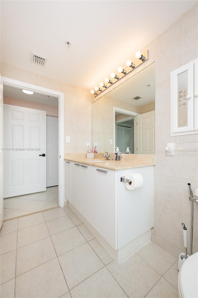 bathroom with tile walls, toilet, vanity, and tile patterned flooring