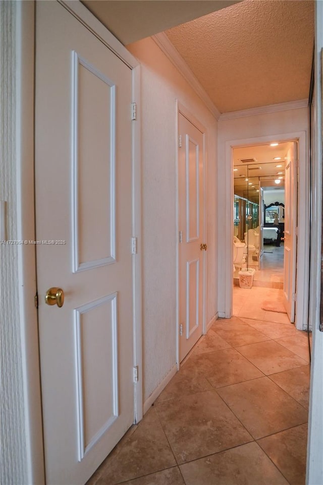 hallway featuring crown molding, light tile patterned flooring, and a textured ceiling