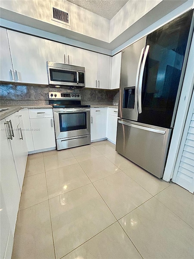 kitchen with light tile patterned floors, white cabinetry, stainless steel appliances, backsplash, and a textured ceiling