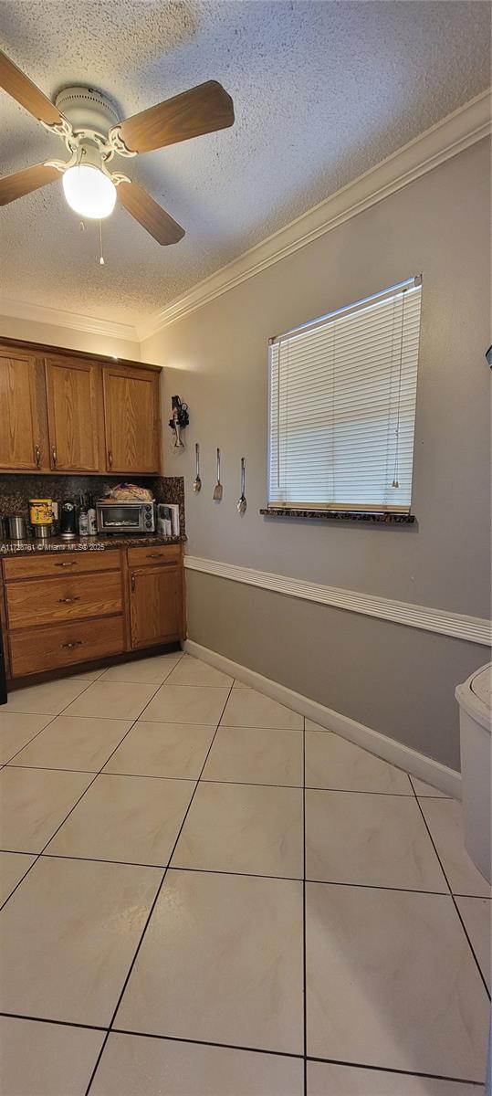 kitchen featuring a textured ceiling, decorative backsplash, ornamental molding, ceiling fan, and light tile patterned floors