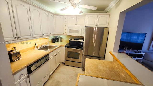 kitchen with ceiling fan, appliances with stainless steel finishes, ornamental molding, white cabinets, and sink