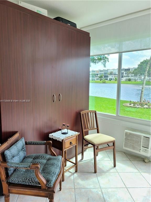 living area with light tile patterned floors, a water view, and a wall mounted air conditioner