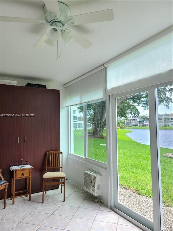 sunroom / solarium with ceiling fan, a wall unit AC, and a water view