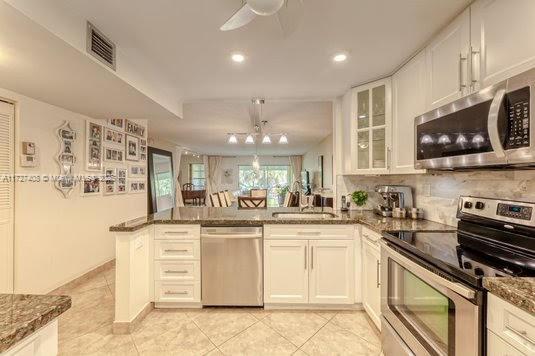 kitchen with white cabinets, appliances with stainless steel finishes, dark stone counters, sink, and kitchen peninsula