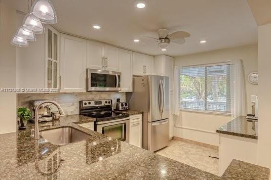 kitchen with sink, dark stone countertops, stainless steel appliances, and white cabinetry