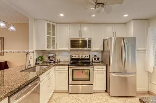 kitchen featuring sink, dark stone countertops, stainless steel appliances, and white cabinetry