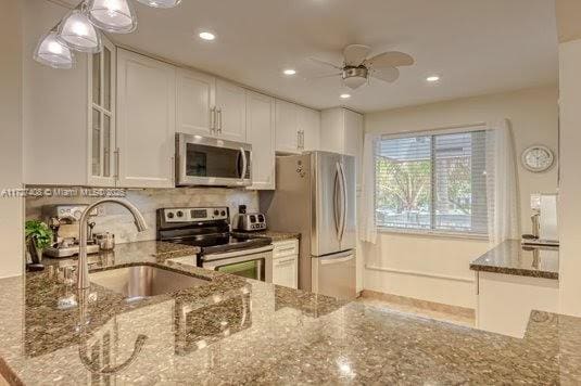 kitchen featuring white cabinetry, ceiling fan, appliances with stainless steel finishes, stone countertops, and sink