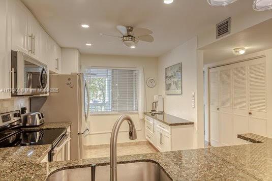 kitchen featuring white cabinetry, ceiling fan, stainless steel appliances, light stone counters, and sink