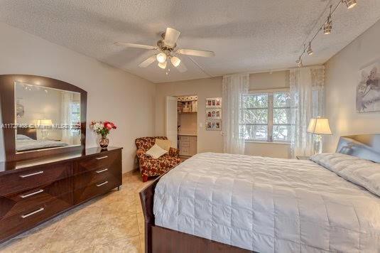 tiled bedroom with ceiling fan, rail lighting, and a textured ceiling