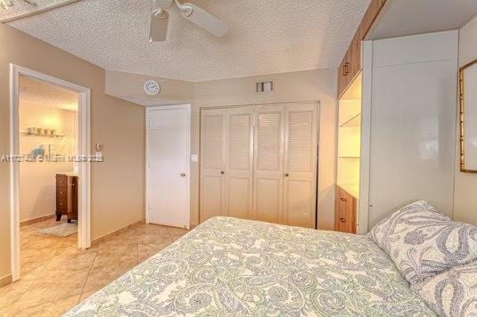 bedroom with ceiling fan, a closet, light tile patterned flooring, and a textured ceiling