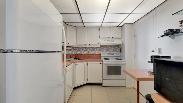 kitchen with a drop ceiling, tile countertops, sink, light tile patterned flooring, and white appliances