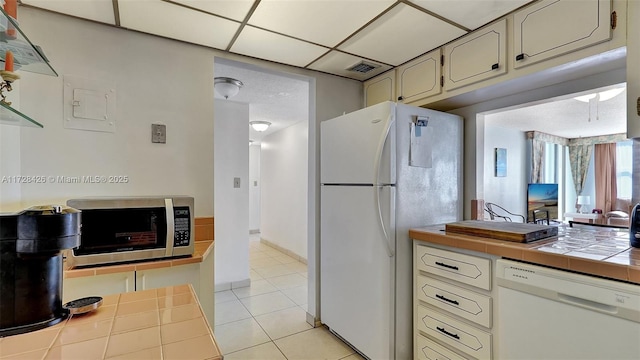 kitchen featuring electric panel, white appliances, a paneled ceiling, tile counters, and light tile patterned floors