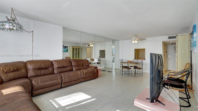 living room with a textured ceiling, ceiling fan, and light tile patterned floors