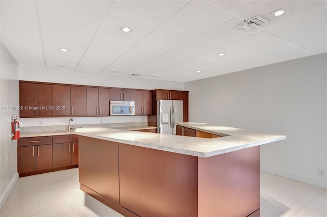 kitchen featuring sink, a drop ceiling, appliances with stainless steel finishes, and an island with sink