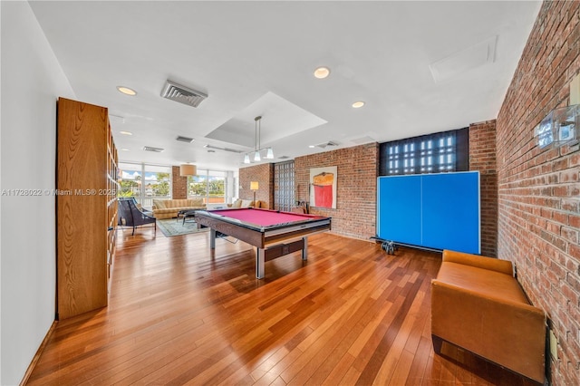 rec room featuring brick wall, light hardwood / wood-style floors, a raised ceiling, and billiards