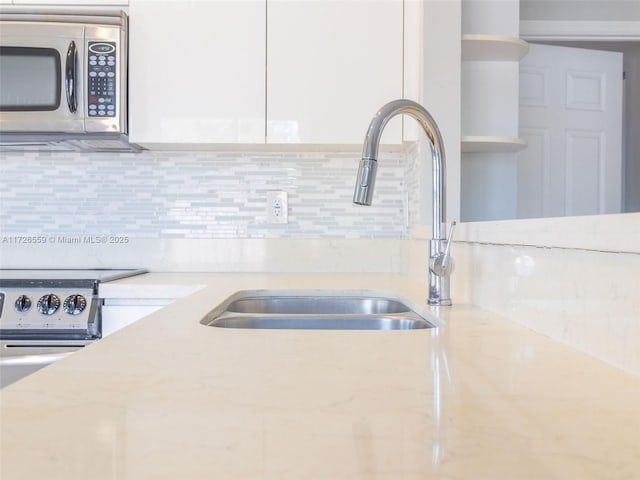 kitchen with sink, light stone counters, white cabinets, and backsplash