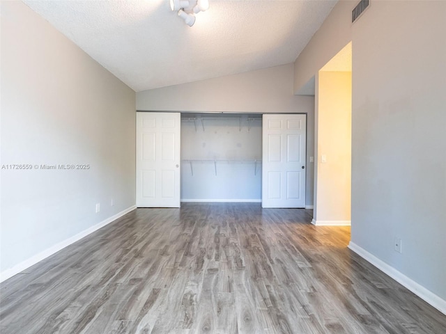 unfurnished bedroom with lofted ceiling, hardwood / wood-style flooring, a closet, and a textured ceiling