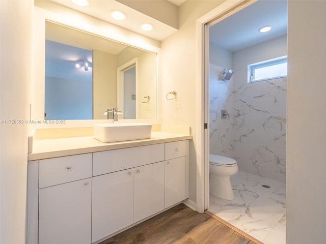 bathroom with vanity, wood-type flooring, a tile shower, and toilet