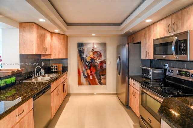 kitchen with appliances with stainless steel finishes, a raised ceiling, tasteful backsplash, dark stone countertops, and sink