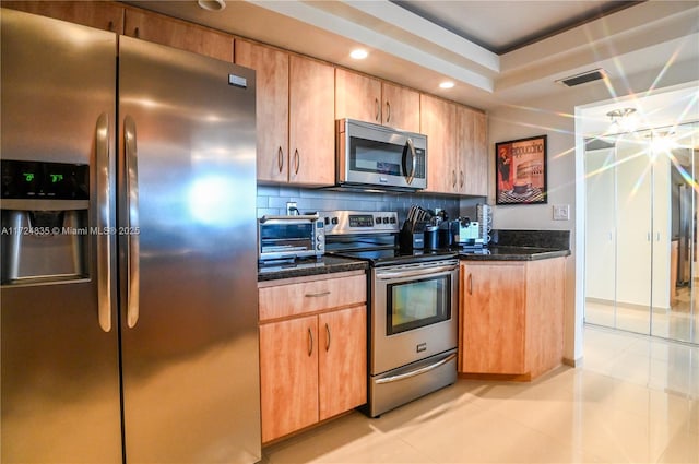 kitchen with light tile patterned floors, backsplash, appliances with stainless steel finishes, and dark stone counters