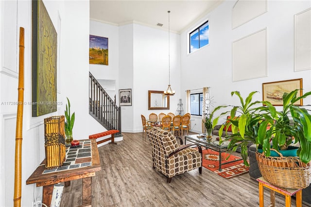 living room with a high ceiling, wood-type flooring, ornamental molding, and a chandelier