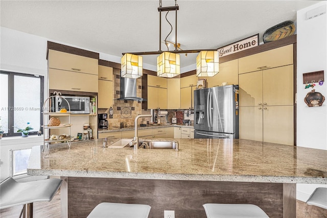 kitchen featuring decorative light fixtures, sink, a kitchen breakfast bar, stainless steel appliances, and wall chimney exhaust hood