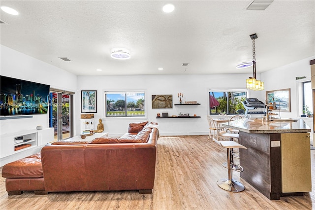 living room with a textured ceiling, an inviting chandelier, light hardwood / wood-style flooring, and sink