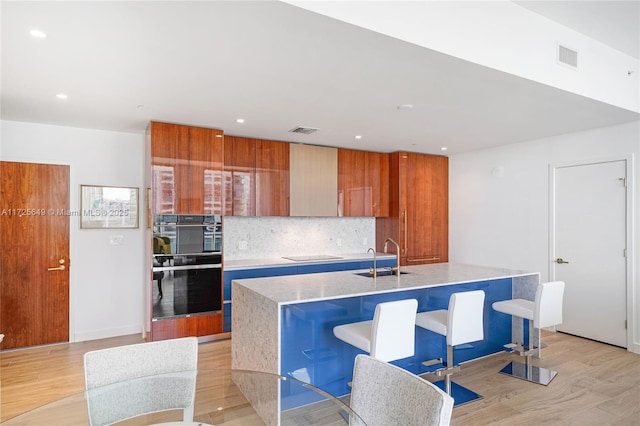 kitchen with decorative backsplash, sink, black appliances, and an island with sink