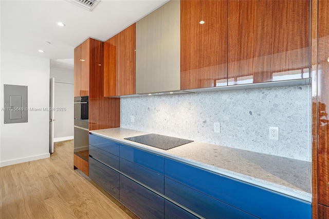 kitchen with black electric stovetop, tasteful backsplash, oven, light stone countertops, and light hardwood / wood-style flooring