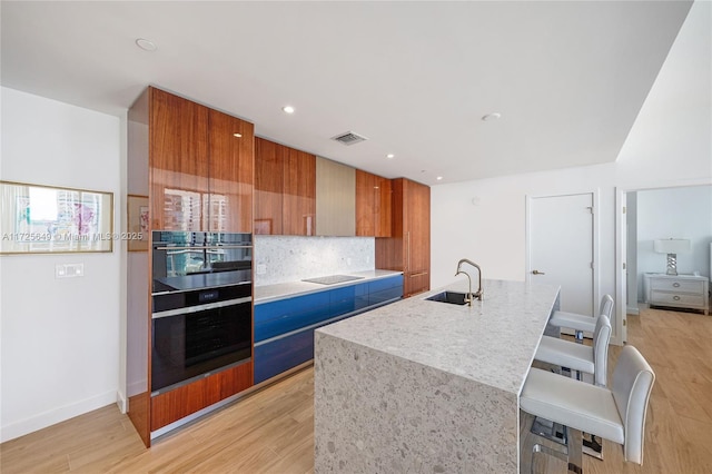 kitchen with a center island with sink, a breakfast bar area, backsplash, sink, and black appliances