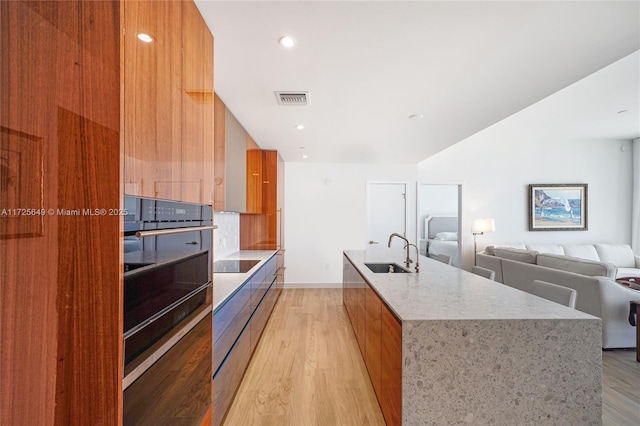 kitchen with light hardwood / wood-style floors, an island with sink, backsplash, black appliances, and sink