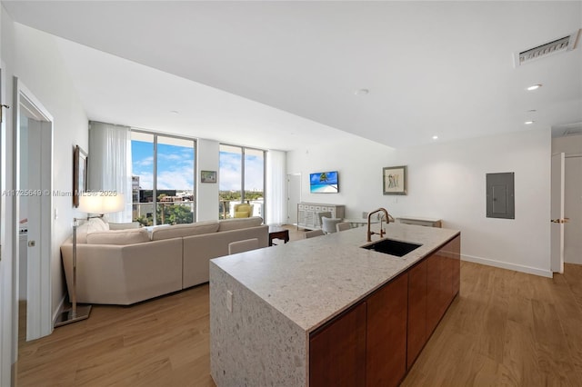 kitchen featuring electric panel, light hardwood / wood-style floors, an island with sink, and sink