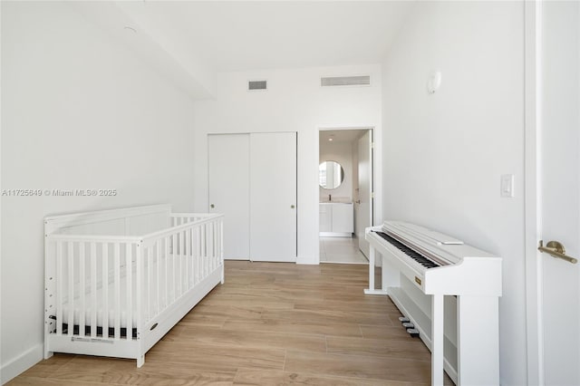 bedroom featuring ensuite bathroom, a nursery area, a closet, and light hardwood / wood-style flooring