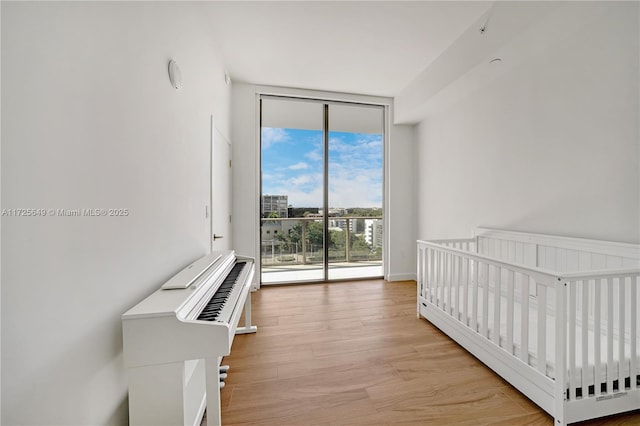 bedroom with light hardwood / wood-style floors, floor to ceiling windows, and a crib