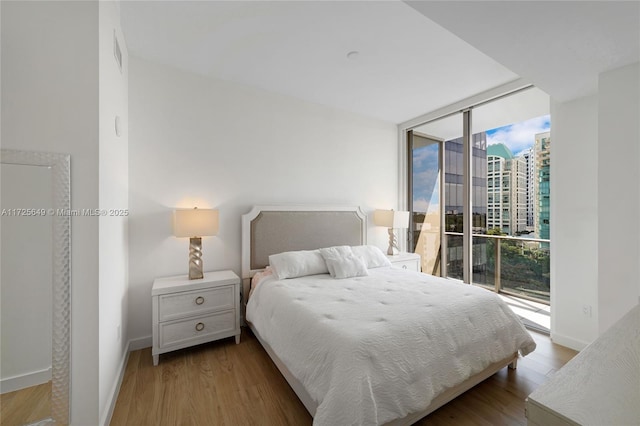 bedroom featuring light wood-type flooring, a wall of windows, and access to exterior