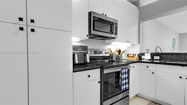 kitchen with sink, white cabinetry, stainless steel appliances, light tile patterned floors, and dark stone counters