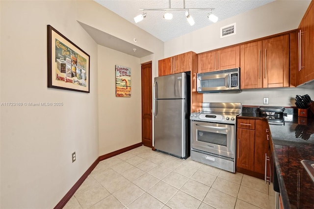 kitchen featuring a textured ceiling, brown cabinetry, light tile patterned flooring, stainless steel appliances, and visible vents