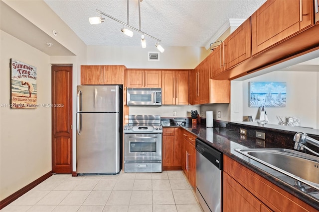 kitchen with brown cabinets, light tile patterned floors, stainless steel appliances, and a sink