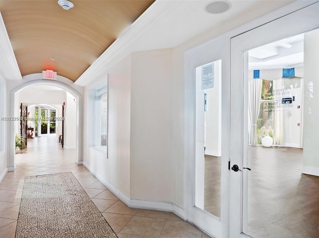 corridor with light tile patterned floors, baseboards, arched walkways, vaulted ceiling, and french doors