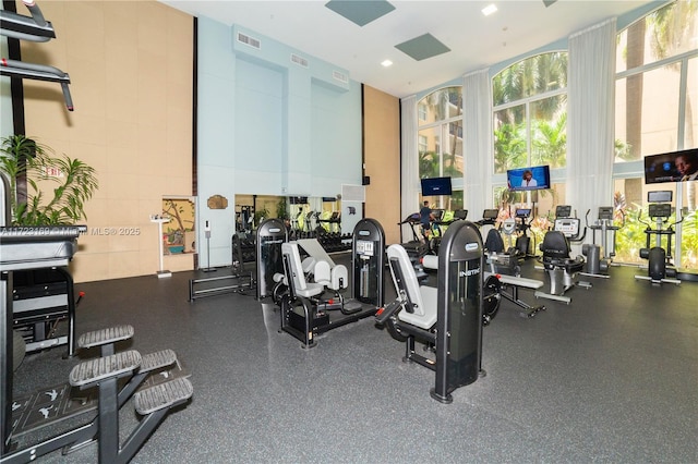 gym with a wall of windows, visible vents, and a high ceiling