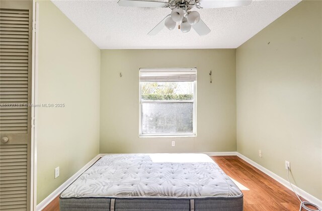 bedroom featuring ceiling fan, wood-type flooring, a closet, and a textured ceiling