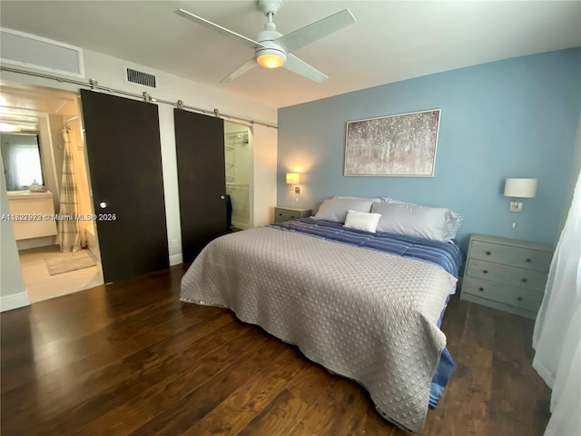 bedroom featuring ceiling fan, a barn door, dark hardwood / wood-style flooring, and ensuite bathroom